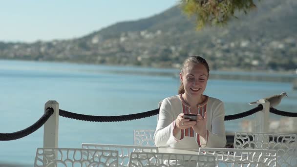 Giovane ragazza scrive SMS in un caffè sulla spiaggia — Video Stock