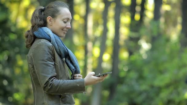 Joven chica escribe SMS en el parque — Vídeo de stock