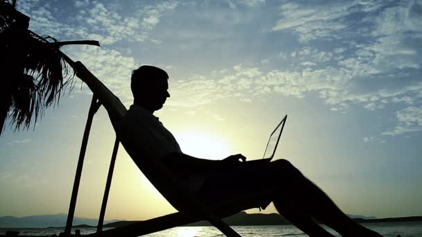 Silueta hombre usando el ordenador portátil en la puesta del sol — Vídeo de stock