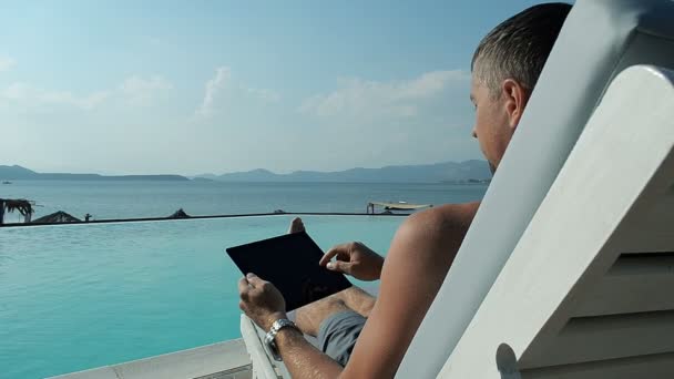 Hombre joven usando la tableta cerca de la piscina — Vídeos de Stock