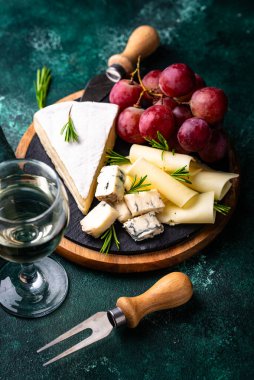 Bir bardak şarap, değişik türde yumuşak peynir ve üzümler.