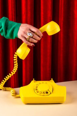 Kırmızı arka planda eski bir telefonu tutan lüks bir kadın.