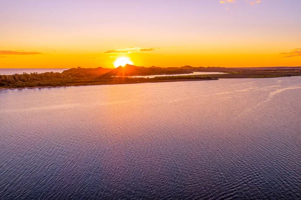 Orange sun touching the hill on horizon with water on foreground and copy space - aerial view