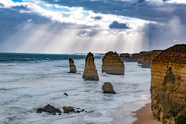 Крупный план скальных образований 12 апостолов под солнечными лучами и бурным небом в Виктории, Австралия
