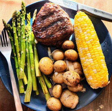 Kuşkonmaz, mısır ve kızarmış patatesli ızgara biftek.