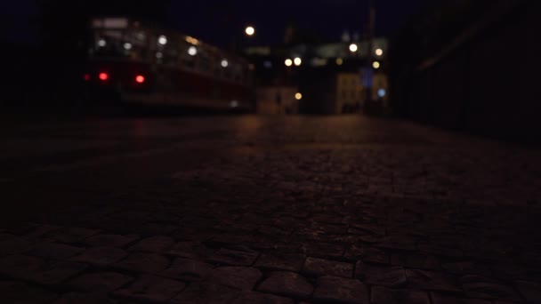 石畳の歩道を歩く歩行者と プラハの中心部の夜に路面電車が通過し 照明が背景に輝きます — ストック動画