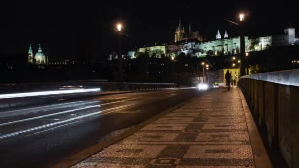 歩道の石畳や夜間の移動中の車やライトの道路背景には夜のチェコ共和国のプラハ城があります — ストック動画