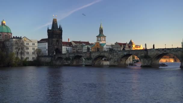 pohybující se záběr na Karlův most a tekoucí řeku Vltavu ve středu Prahy při západu slunce obloha je v České republice modrá