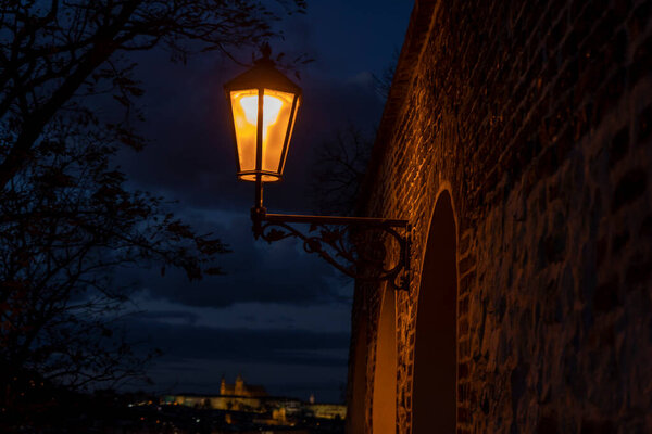 Light from street lights and the old stone walls of the fortress from the 15th century and paving stones on the ground for pedestrians at night in the center of Prague in the Czech Republic in autumn
