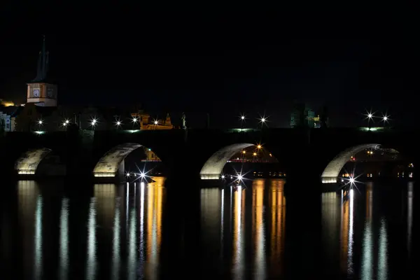 illuminated Charles Bridge from 14 centuries and light from street lighting and stone sculptures on the bridge and light reflections on the surface of the Vltava river at night in Prague