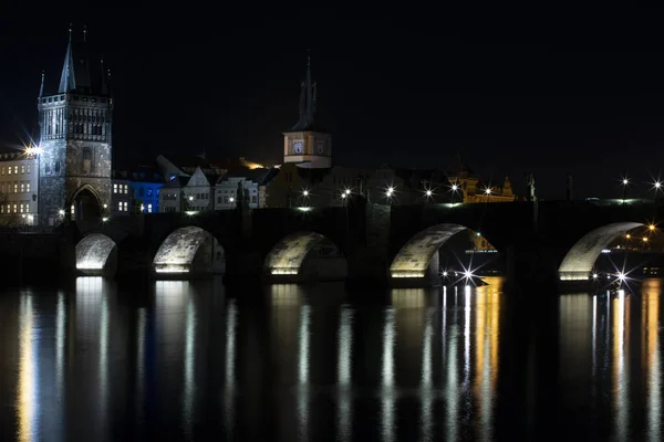 illuminated Charles Bridge from 14 centuries and light from street lighting and stone sculptures on the bridge and light reflections on the surface of the Vltava river at night in Prague