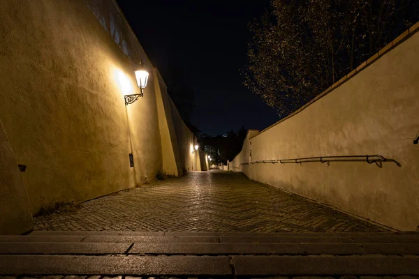 sidewalk with cobblestones for pedestrians and light from street lights in the center of Prague at night