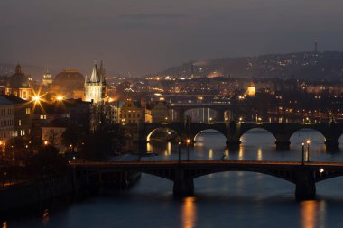 Vltava Nehri 'nin manzarası ve köprüler arasındaki köprüler ve Charles Köprüsü ve çevresindeki mimari ve ışık gün batımından sonra Prag' ın göbeğindeki sokak lambaları.