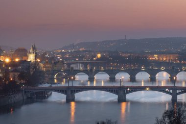 Vltava Nehri 'nin manzarası ve köprüler arasındaki köprüler ve Charles Köprüsü ve çevresindeki mimari ve ışık gün batımından sonra Prag' ın göbeğindeki sokak lambaları.