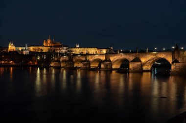 Prag Kalesi ve Charles Köprüsü ve St. Vita Kilisesi ışıkları Prag 'ın merkezindeki Vltava Nehri' nin yüzeyine yansıyor.