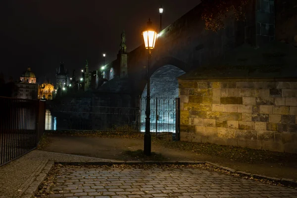 street light lamp and paving sidewalk with cobblestone and lights in the background on Charles Bridge in the center of Prague at night