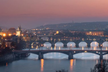 Vltava Nehri 'nin manzarası ve köprüler arasındaki köprüler ve Charles Köprüsü ve çevresindeki mimari ve ışık gün batımından sonra Prag' ın göbeğindeki sokak lambaları.
