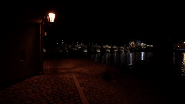 pouliční osvětlení a dlážděný chodník pro pěší a pak noční pohled na Karlův most a jeho osvětlení v noci a tekoucí řeku Vltavu v centru Prahy