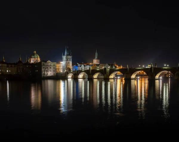 夜のチェコ共和国プラハの中心部にあるカレル橋とライトアップされた街路灯と周辺の古い建築物のパノラマビュー — ストック写真