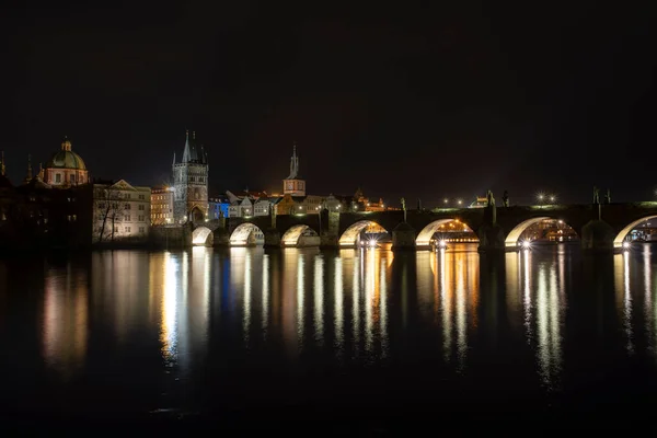 夜のチェコ共和国プラハの中心部にあるカレル橋とライトアップされた街路灯と周辺の古い建築物のパノラマビュー — ストック写真