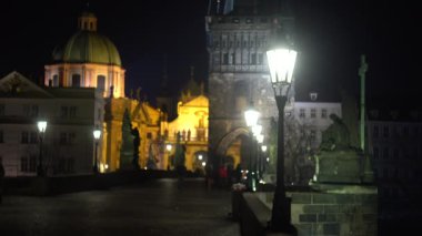 Geceleyin taşın üzerindeki sokak ışıkları ve heykeller ve Prag 'ın merkezinde gece vakti köprüde yürüyen insanların siluetleri ve gökyüzünde uçan kuşlar.
