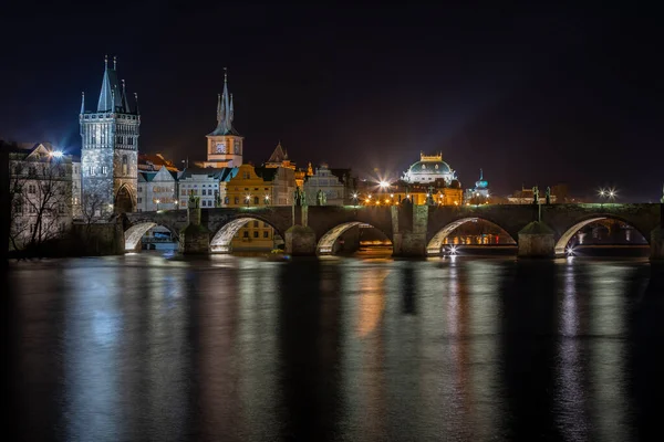 ヴルタヴァ川に架かるチャールズ橋はライトアップされ 夜のプラハ中心部の水面には街路灯の光が反射しています — ストック写真