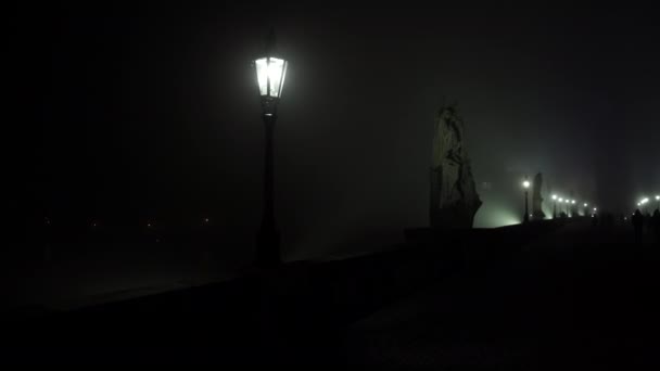 Bewegungsblick Licht in die Laterne der Straßenbeleuchtung auf der Karlsbrücke und Nebel in der Nacht und Silhouetten von Fußgängern und Läufern auf dem Kopfsteinpflaster auf der Brücke im aufsteigenden Nebel in der Nacht.