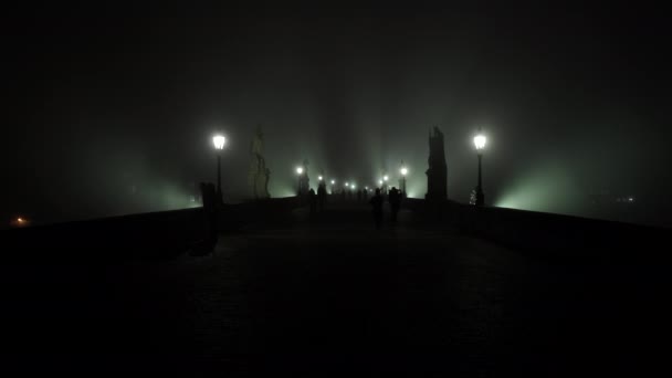 světlo do lucerny pouličního osvětlení na Karlově mostě a mlha v noci a siluety chodců a běžců na dlážděném chodníku na mostě ve stoupající mlze v noci