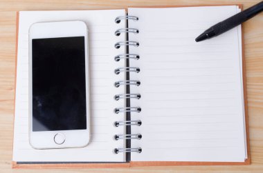 Ahşap arka planda bir defter olan akıllı telefon.