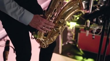 Siyah pantolon ve mavi gömlek giymiş genç beyaz adam müzik aleti saksafon çalıyor, elleri davul ve renkli ışığın arka planında gerekli vanaları kapatıyor. Yakın plan, aksiyon sahneleri.