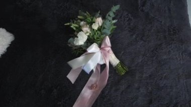 Birbirine aşık mutlu çiftin iki altın alyansı pembe kurdelenin üzerinde yatar. Bu kurdele, gül buketi ve okaliptüs ağacı dalları için bir fiyonk oluşturur. Buket kabarık battaniyenin üzerinde yatıyor.