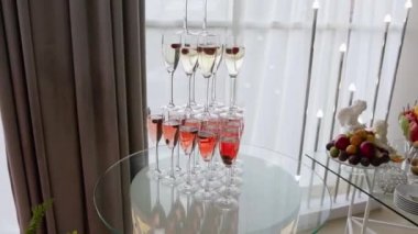 Beyaz ve pembe şampanyalarla dolu ince cam bardaklardan yapılmış üç katlı bir slayt ayakta duruyor ve pahalı ve zarif bir büfenin inceliğini tamamlıyor.
