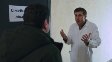 Beyaz önlüklü aile doktoru heyecanlı, kızgın ve endişeli bir şekilde hastaya bağırıyor ve ellerini sallayarak ofisine giriyor.