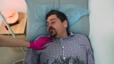 Kafkasyalı hasta bir adam kanepede yatar ve uyur ve kötü bir rüya görür, kafasını farklı yönlere çevirir, ve hemşire onu uyandırıp ilaç sistemini kapatır ve damardan iğneyi çıkarır.
