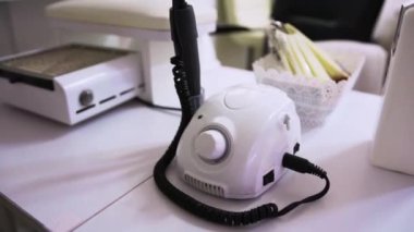 Beyaz renkli manikür için değirmen kesme makinesi, manikür için elektrik süpürgesinin yanında bir masanın üzerinde duruyor ve güzellik salonundaki bir kolluk.