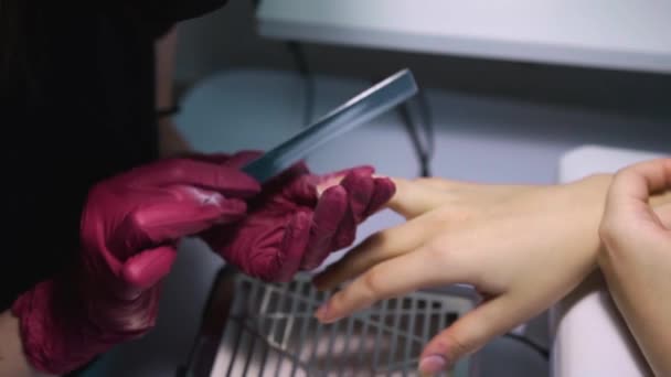 ネイルファイル付き美容室で使い捨てニトリル手袋のマニキュリストは 側面にそれらを見て 爪真空クリーナーの上に正方形の形状を作ることによって クライアントの爪の形状を調整します — ストック動画