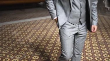 Zarif gri takım elbiseli beyaz gömlekli beyaz bir adam elini pantolonunun cebine sokar ve eski geniş fayanslı bir odada merdivenleri tırmanır.
