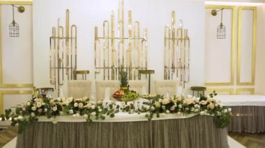 Masa örtüsüyle kaplı büyük bir masa, çatal bıçaklar, bardaklar ve meyvelerle servis edilir ve taze çiçek kompozisyonu ile süslenir. Restoranda beyaz duvarlara karşı modern dekorlarla süslenir.