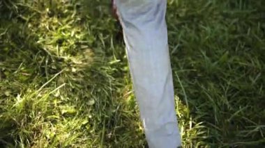 Gri zarif takım elbiseli ve kahverengi ayakkabılı beyaz bir adam taze yeşil çimlerde yürüyor ve beyaz şakayık demeti taşıyor.