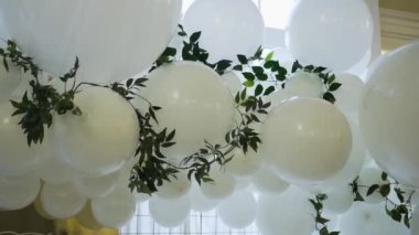 Farklı boyutlarda, büyük ve küçük bir sürü beyaz balonla, yeşil sarmaşık bitkisinin dallarından ve kare altın tabelasıyla, nefis bir düğün kemeri.