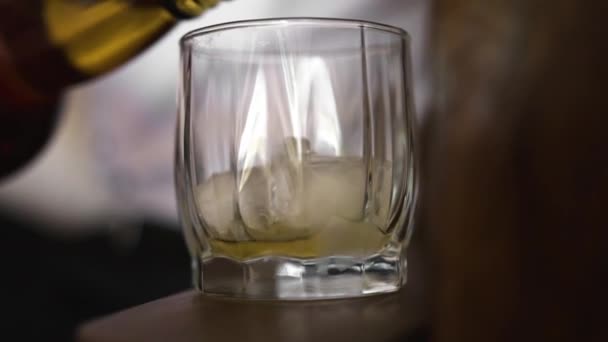 房间里站着一个干净透明的装有冰块的杯子 有人从瓶子里往里面倒了一杯浓烈的棕色酒精饮料 — 图库视频影像