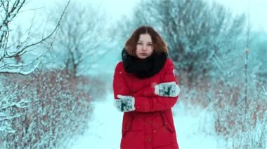 Upset, frustrated, tired and frozen cute girl stands in snow between trees and bushes in winter and shivers from cold and steps from foot to foot and rubs her gloved hands and give her body warmth
