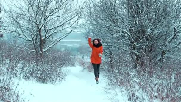 フレンドリーで幸せな若い白人の少女は 冬には屋外で木々や茂みの間の雪の道を走り ニット手袋で手を明るく積極的に振って言います こんにちは — ストック動画