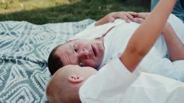 Beyaz bir baba ve oğul parkta bir battaniyeye aynı şekilde giyinmiş ve ciddi bir konu hakkında konuşuyorlar. Babam çocuğa bir şey söyler ve öğretir. Aile terbiyesi