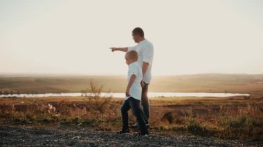 Baba oğul gün batımında yürür ve baba çocuğa öğretir. Ebeveyn küçük bir adam yetiştirir ve uzaktan bir şey gösterir. İlgilenen çocuk dikkatlice yetişkinleri dinler ve bir şey sorar.