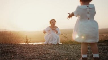 Küçük bebek kız gün batımında altın tarlada yürümeye başlıyor ve anne ve kızının siluetine uzanan elleri, başını sallayan mutlu, güler yüzlü annesine gidiyor.