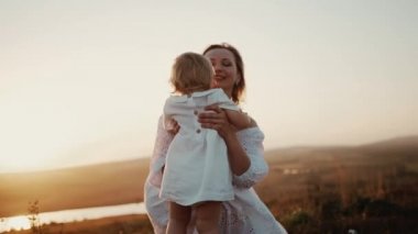 Mutlu, güzel bir aile. Çocuk kucağa koşuyor anne kucağa tatlı küçük kızını kaldırıyor ve gün batımında tarlada kendi etrafında dönüyor, komik kız annesinin kollarında uçuyor birlikte gülüyor, eğleniyor.