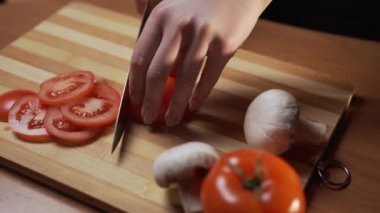 Şef organik çiğ sebzeleri ince dilimlere ayırır. Tahta üzerinde keskin metal bir bıçakla dilimlenen kırmızı sulu domateslerin hazırlanma süreci.