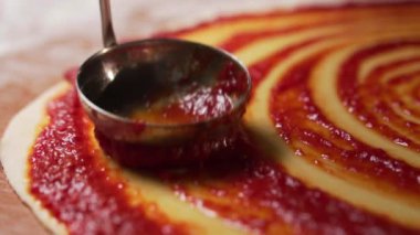 Şef lezzetli bir geleneksel İtalyan pizza yemeği hazırlar ve domates sosunu demir kaşıkla yuvarlak hamura yayar. Kapat.