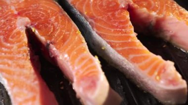 Çiğ kırmızı balık parçaları elektrikli ızgaranın üzerinde yatıyor. Somon biftekleri misafirler için hazırdır. Yüksek sıcaklıktan dolayı aşırı ısınan yağlar ve gurultular kabarcıklar oluşturuyor. Yakın plan.